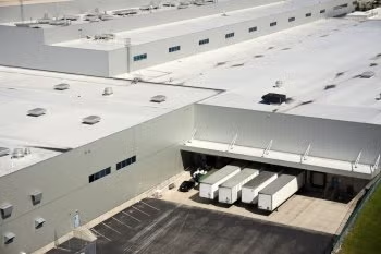 Aerial view of a large white warehouse with several delivery trucks parked at loading docks.