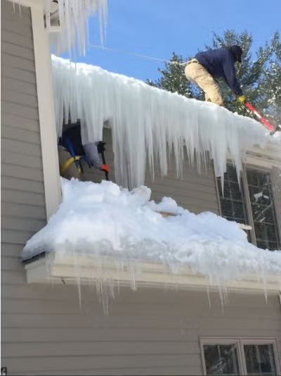 Person clearing heavy icicles and snow from a house roof in winter