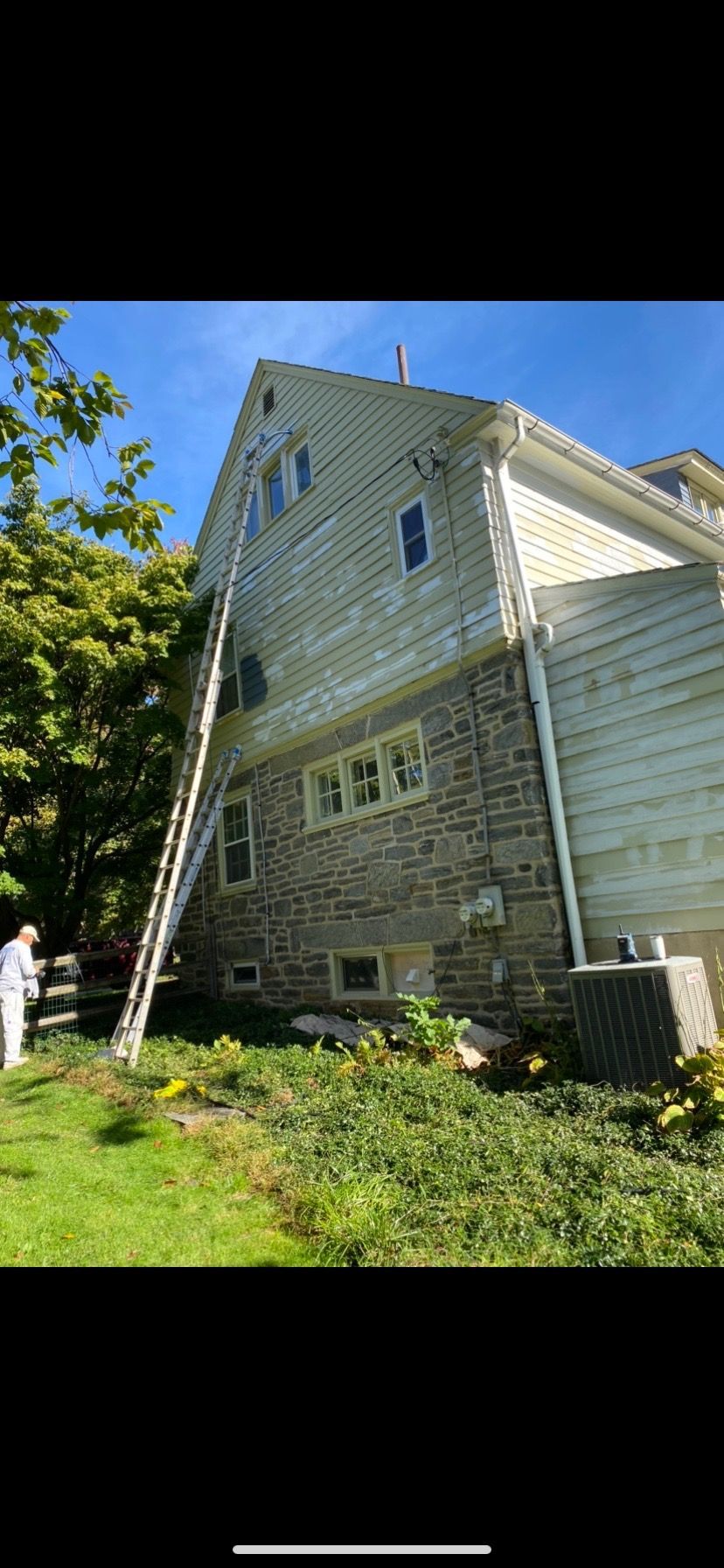 A man is painting the side of a house with a ladder.