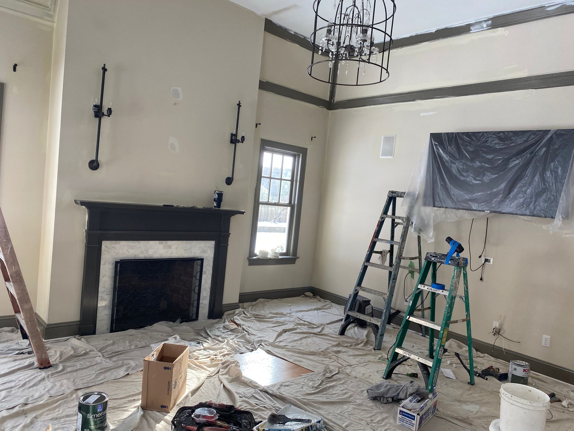 A living room is being painted with a fireplace and ladder.