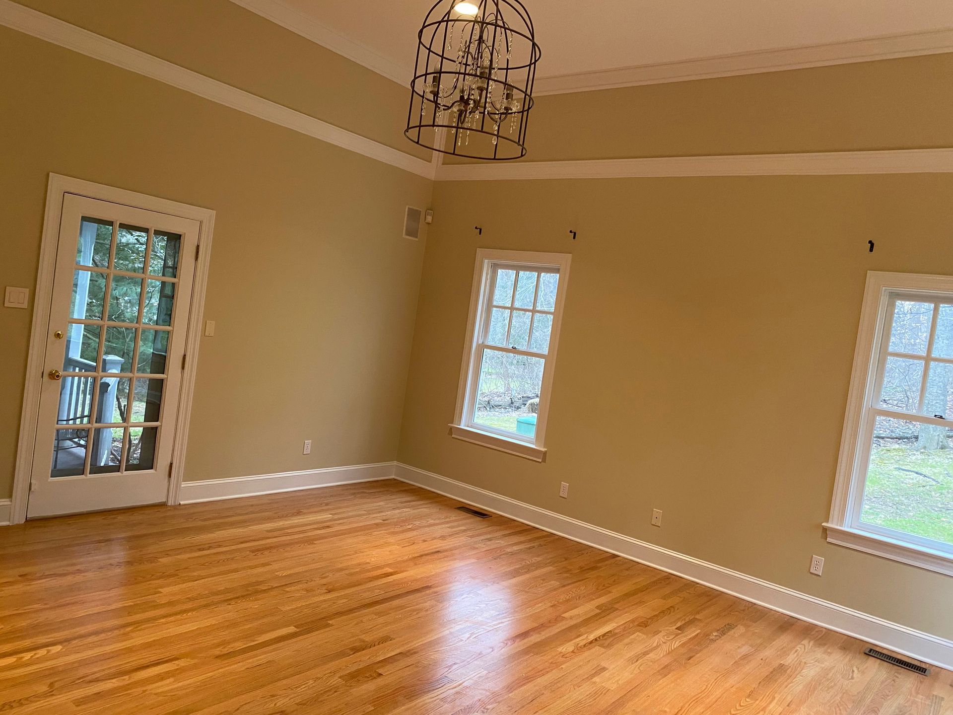 An empty living room with hardwood floors and a chandelier hanging from the ceiling.