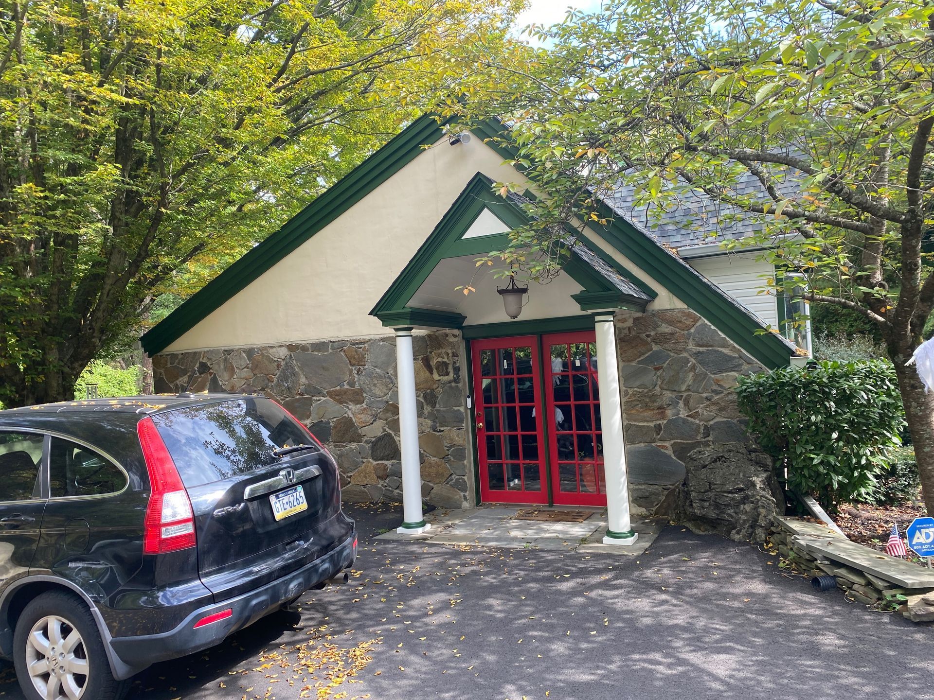 A black car is parked in front of a stone building with red doors.