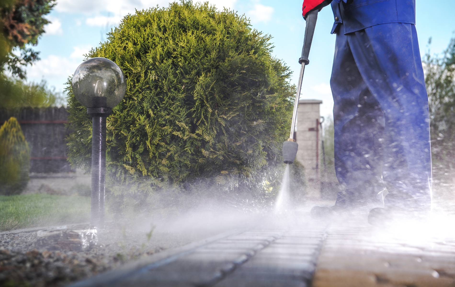 A man is using a high pressure washer to clean a brick walkway.