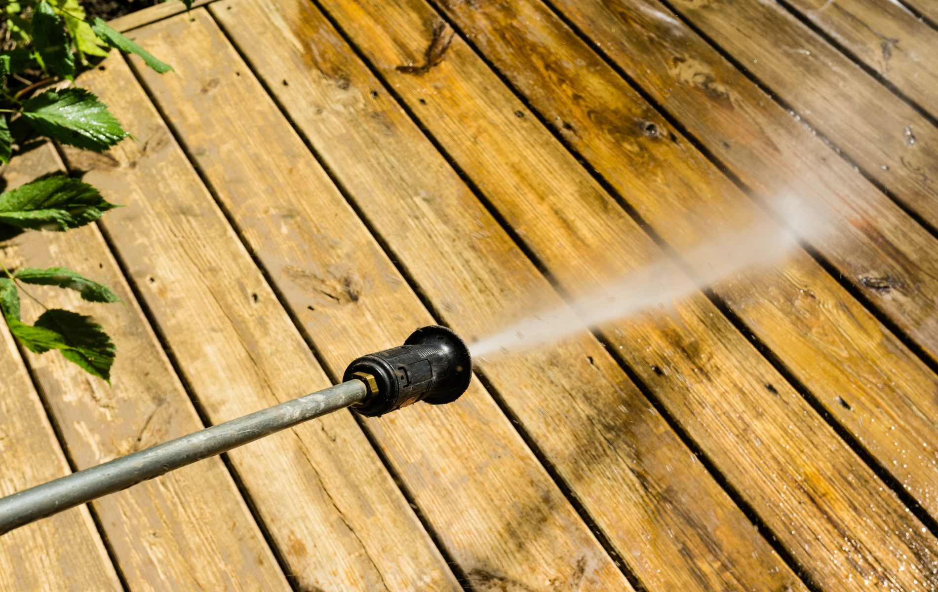 A person is using a high pressure washer to clean a wooden deck.