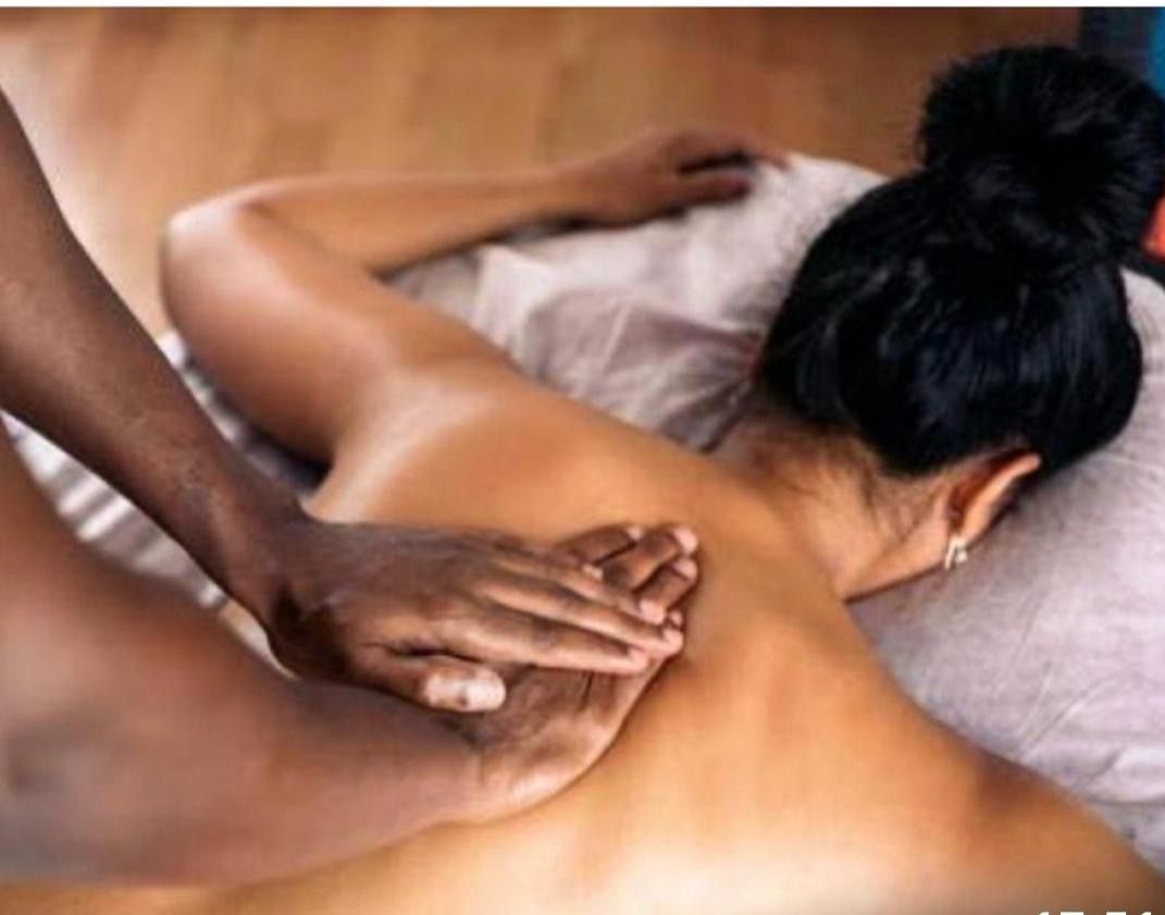 En person i en blå skjorte masserer ryggen af en person, der ligger med ansigtet nedad på en massagebriks udendørs.