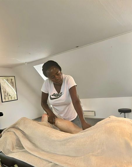 En person i en blå skjorte masserer ryggen af en person, der ligger med ansigtet nedad på en massagebriks udendørs.