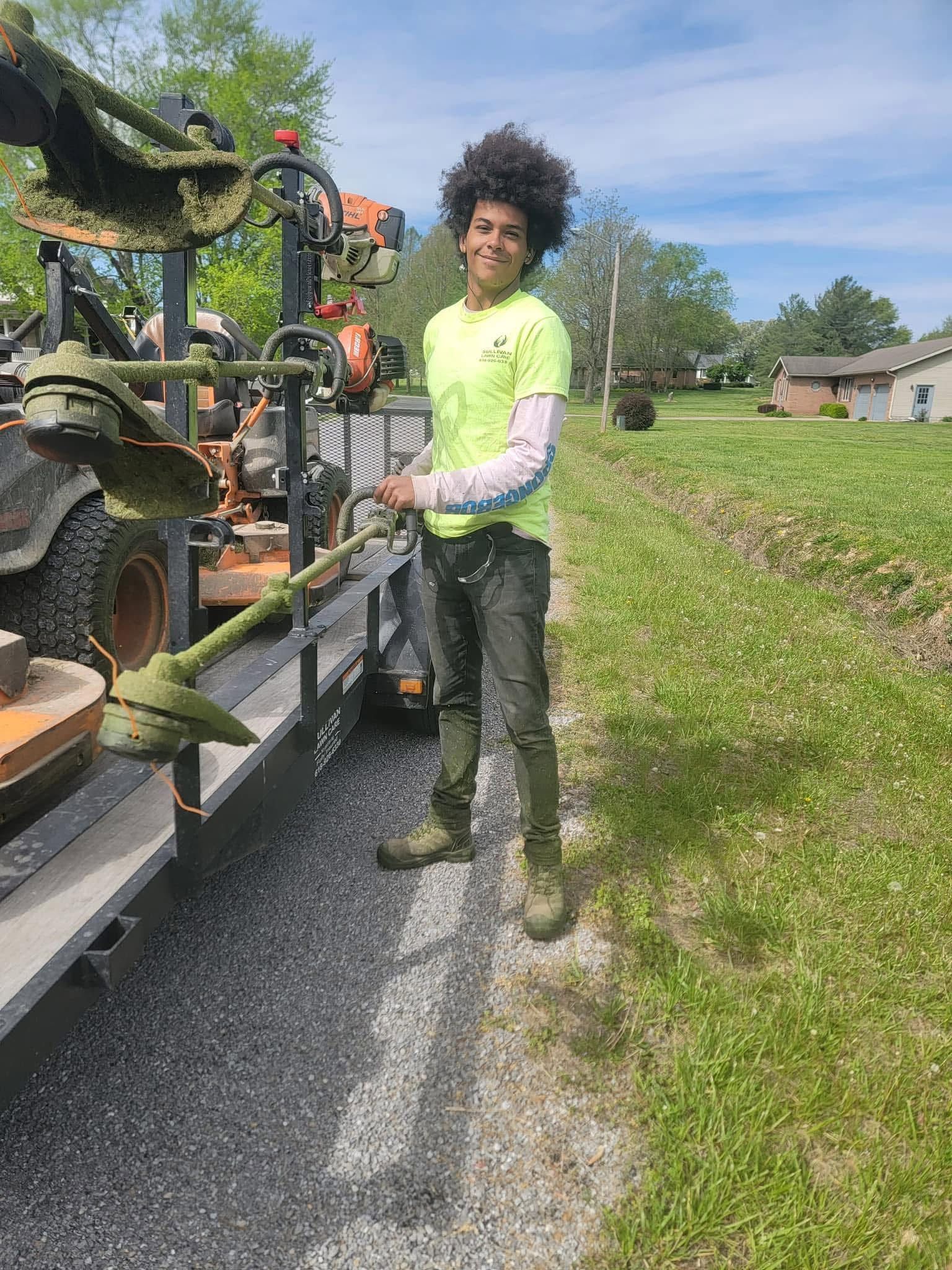 Person in neon green shirt holding a tool beside a trailer loaded with equipment on a rural road.