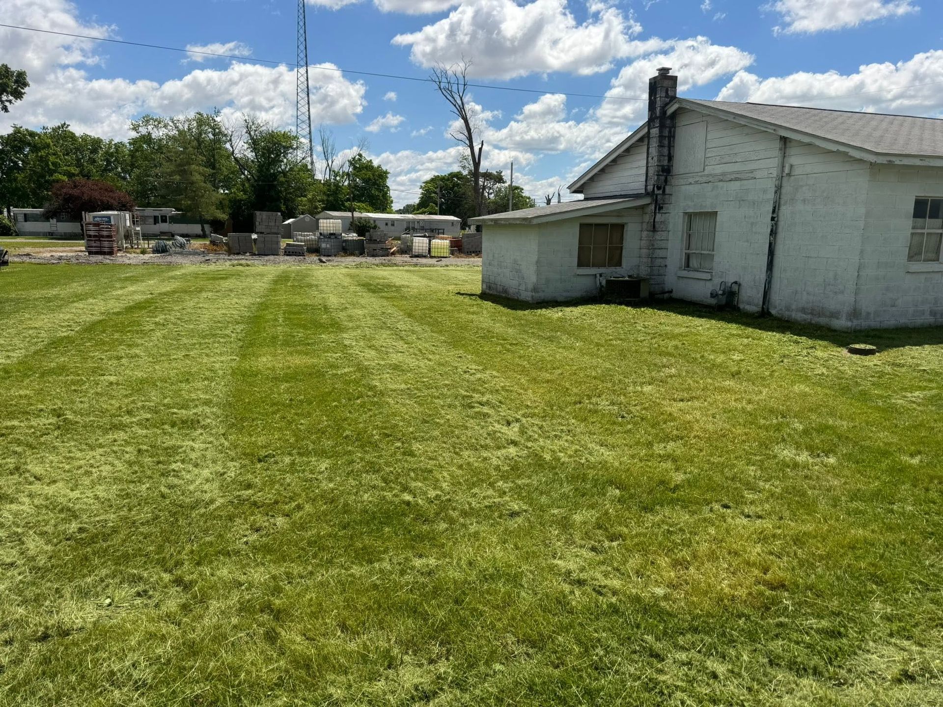 Mowed grassy yard beside a white house under a partly cloudy sky