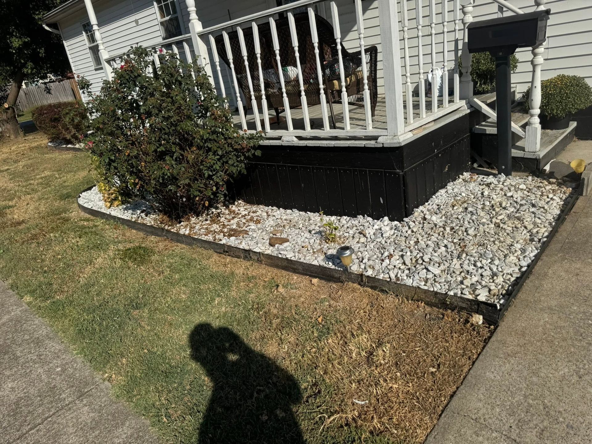 Front porch with white railing, gravel bed, shrubs, and a concrete walkway beside a lawn.