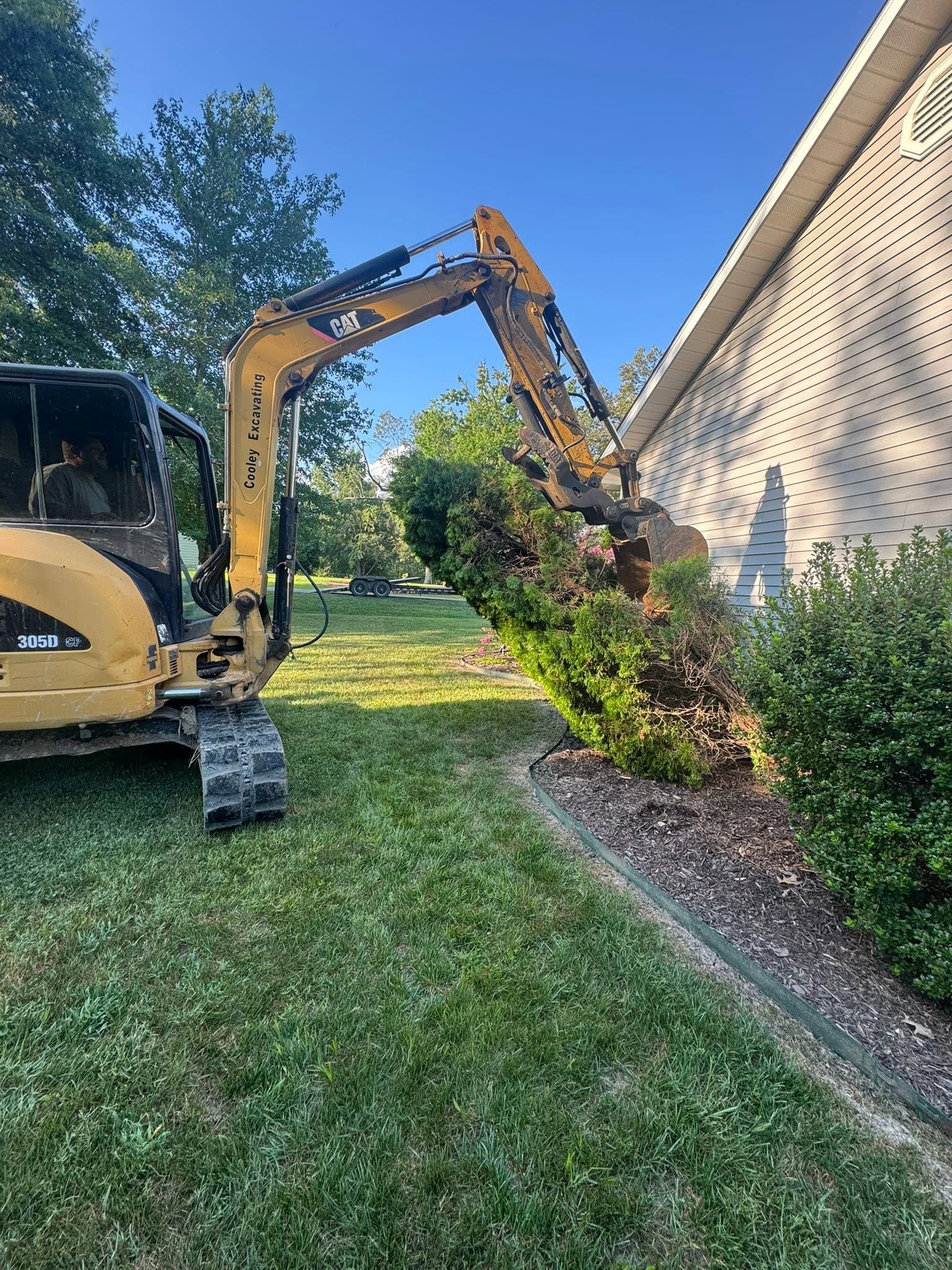 Excavator trimming bushes beside a house on a sunny lawn