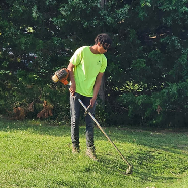 Person using a grass trimmer on a sunny lawn, wearing a neon green shirt.