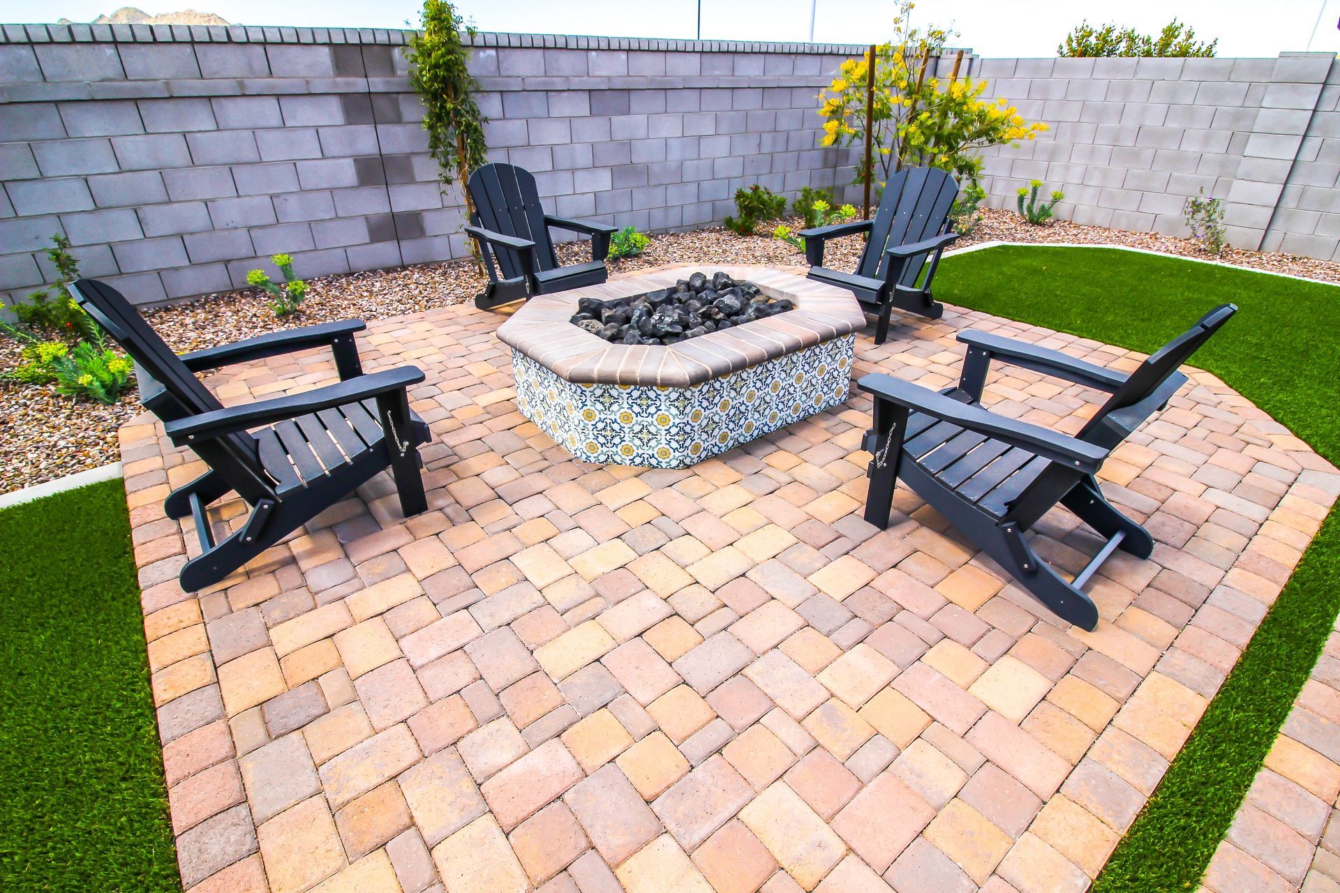 Patio fire pit surrounded by black chairs on a brick paver seating area with a cinder block wall backdrop