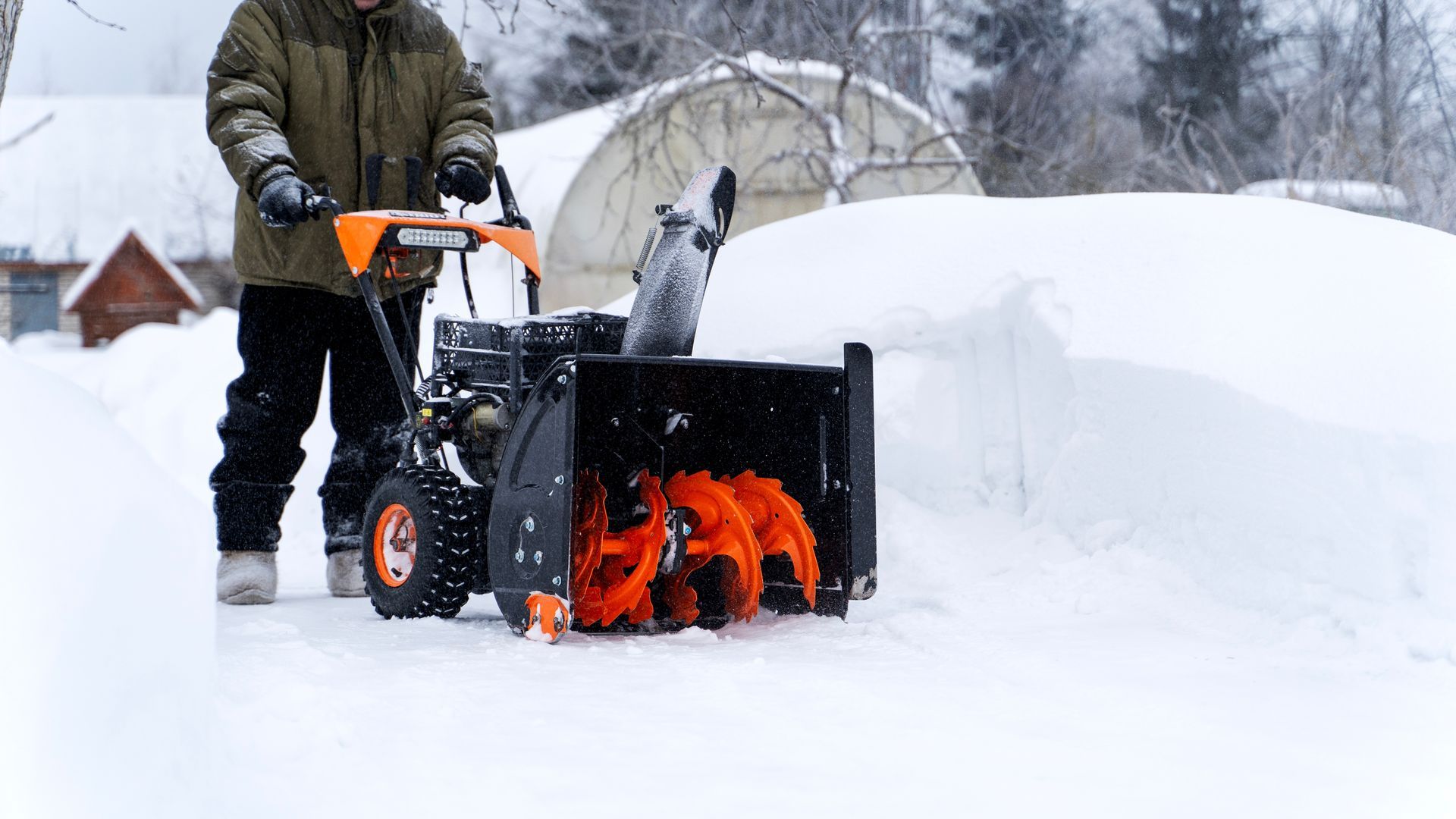 Person using an orange snow blower clearing deep snow in a snowy yard