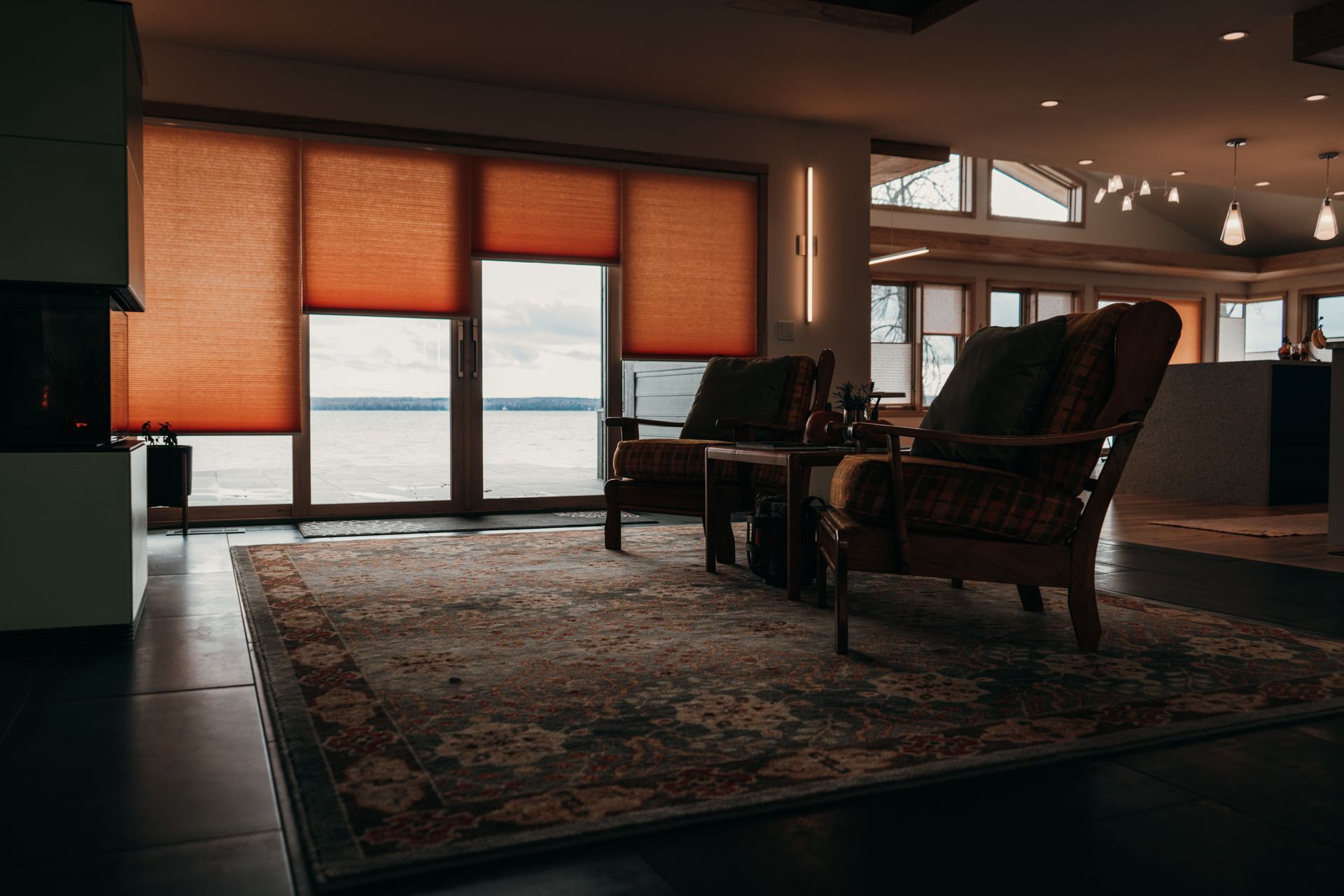Cozy lounge with wicker chairs, patterned rug, and large windows with orange shades overlooking water