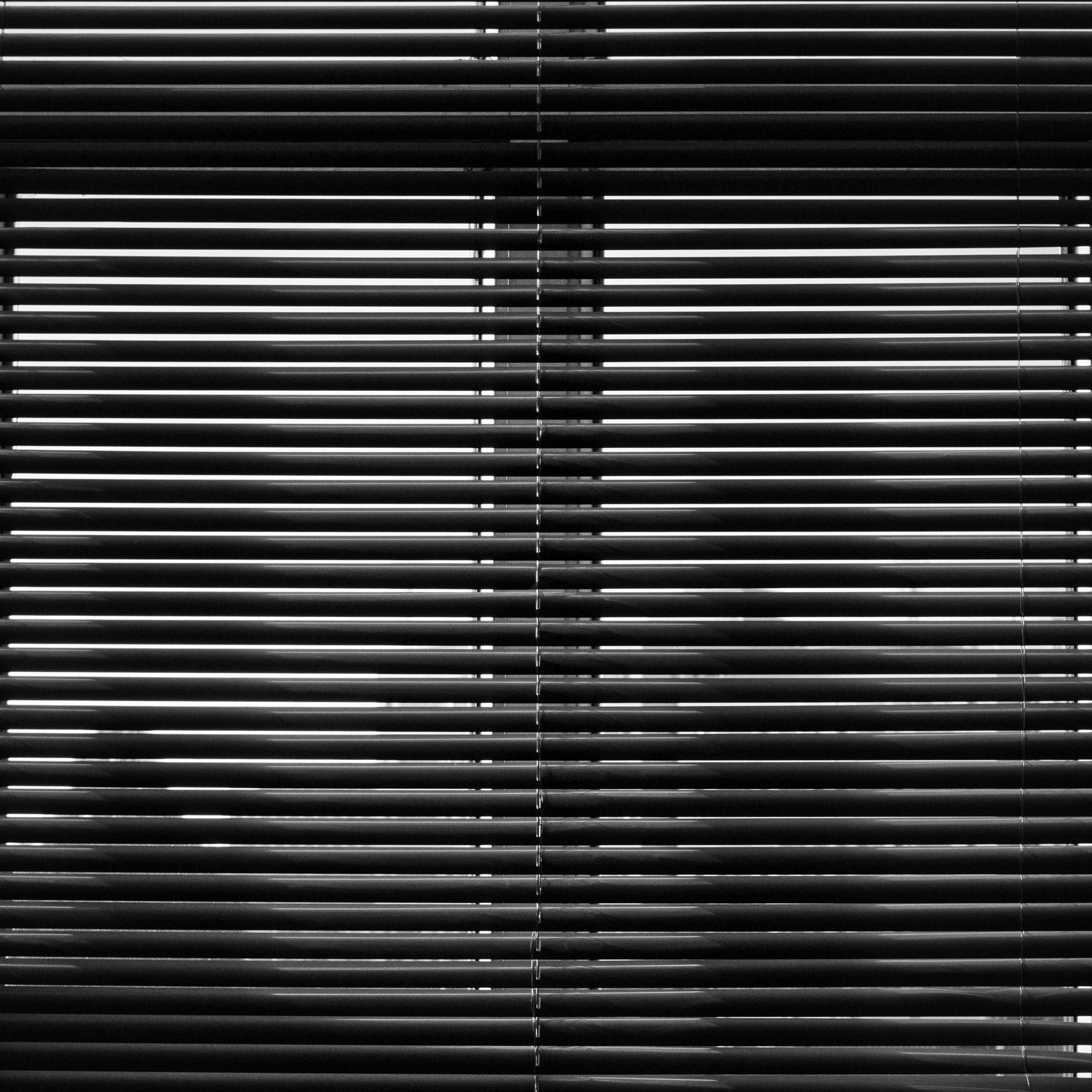 Closed black window blinds with a thin line of light showing through the slats