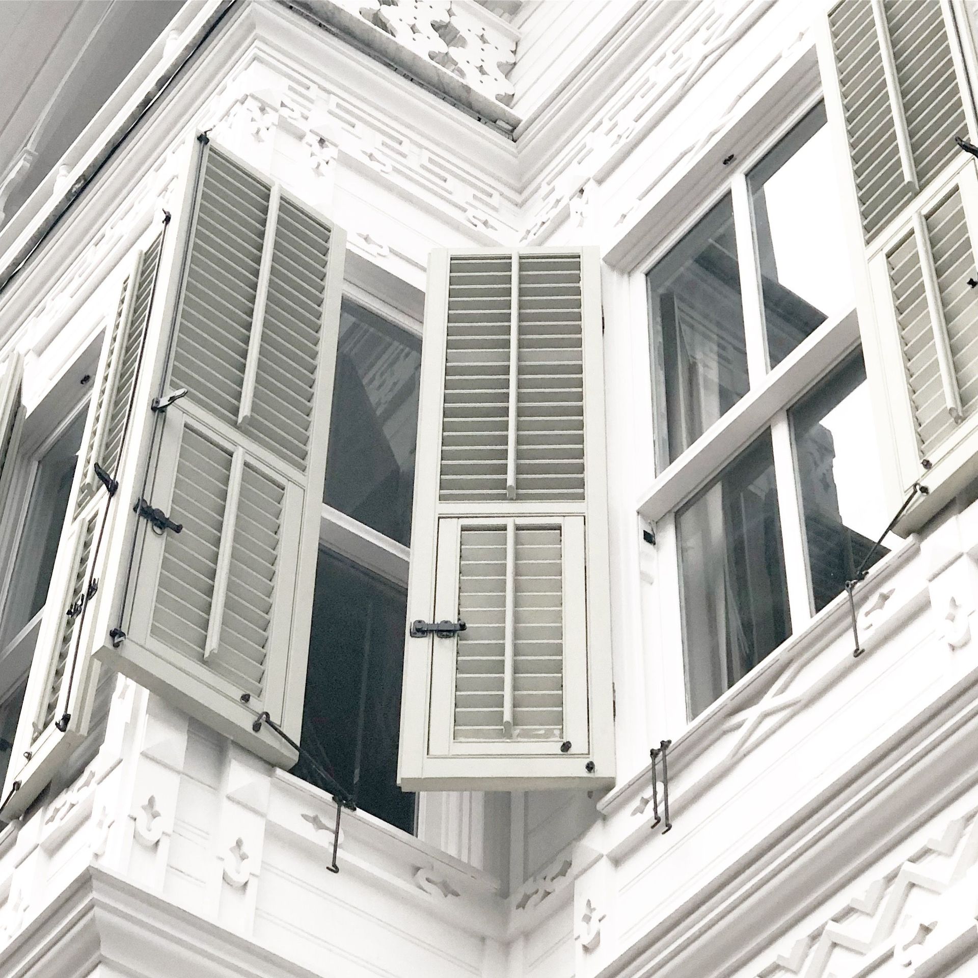 White house corner with open gray shutters and tall windows viewed from below