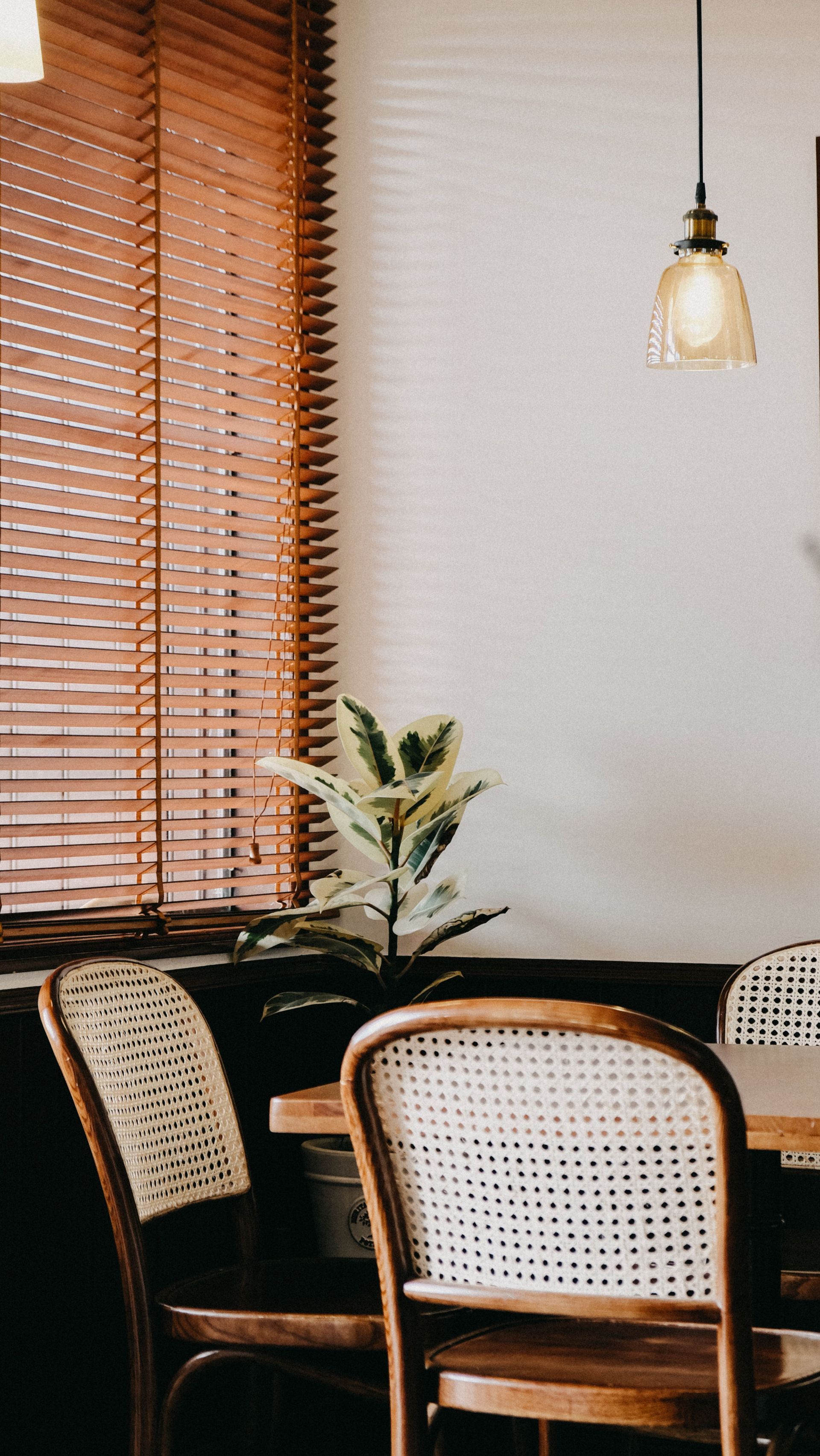 Cozy cafe corner with woven chairs, wooden table, hanging pendant light, and window blinds