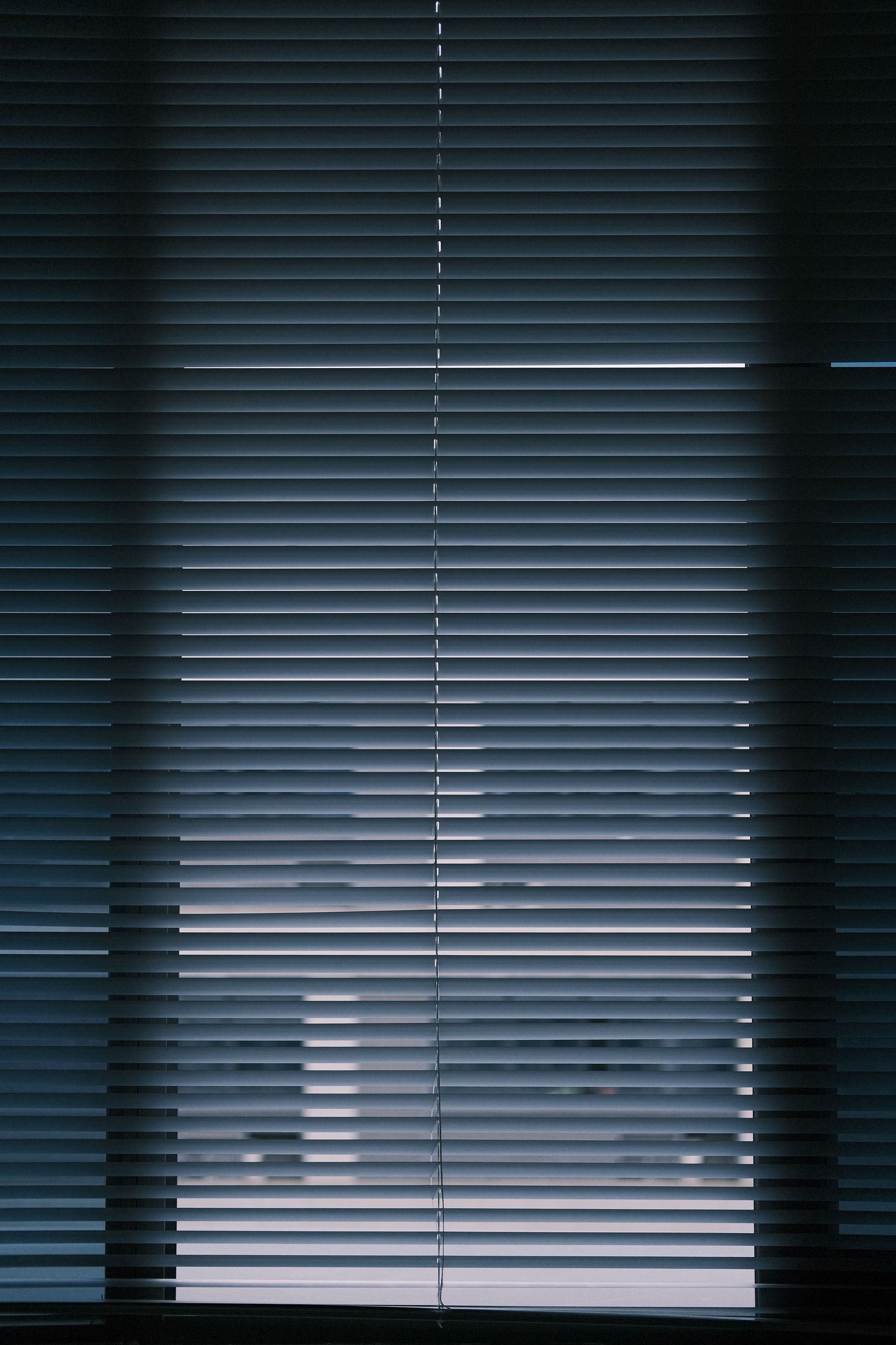 Closed venetian blinds with dim blue light filtering through a window