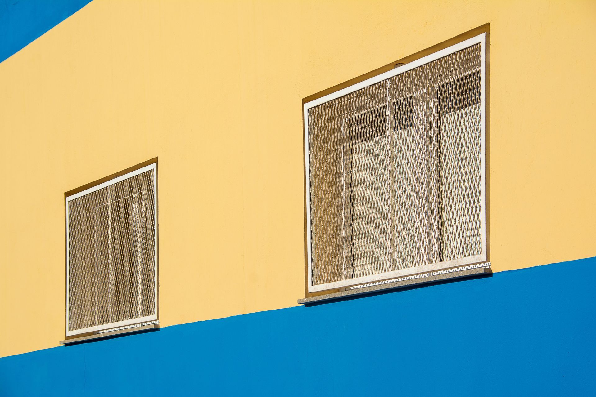 Two barred windows on a yellow and blue building wall