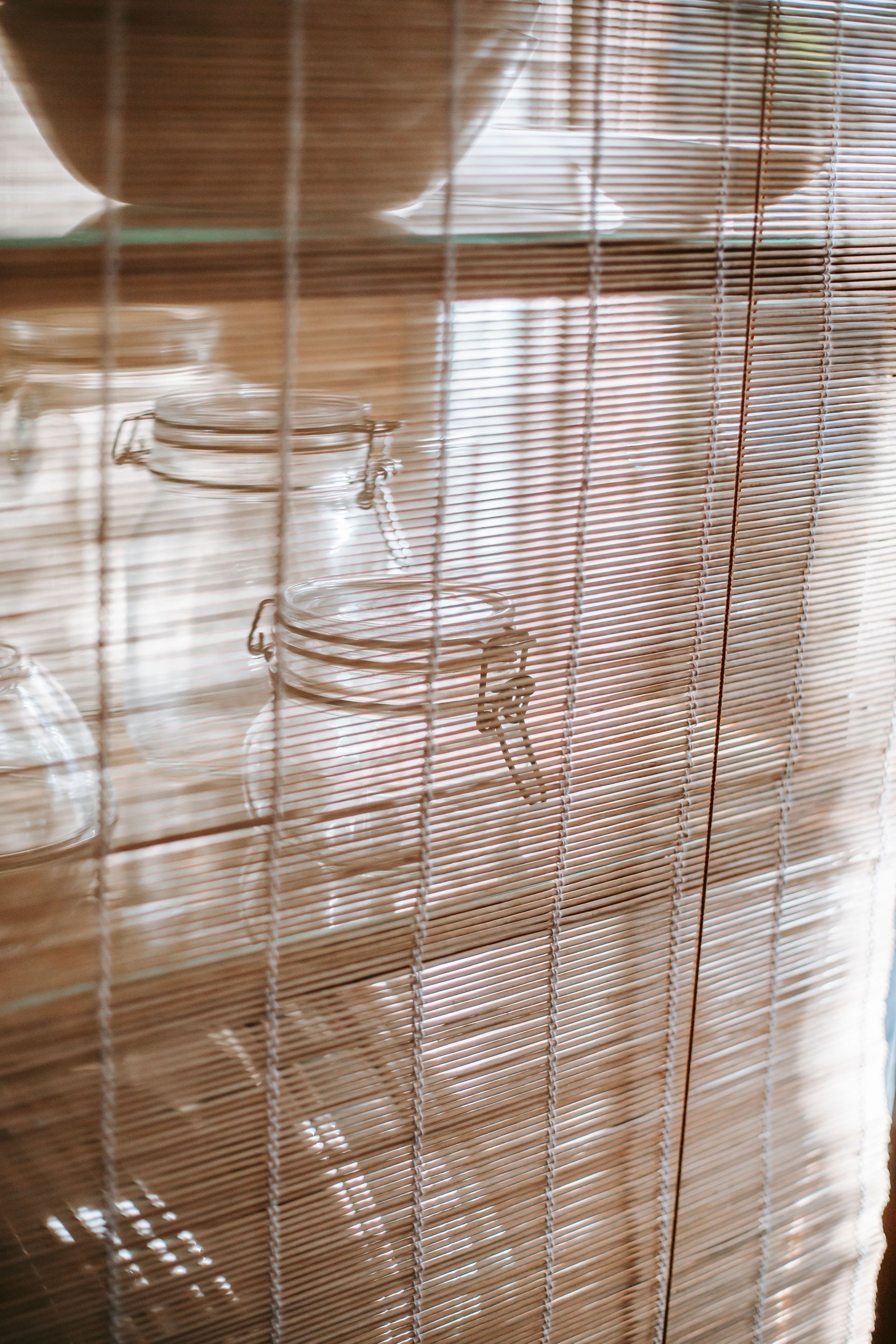 Woven bamboo blinds filtering sunlight, with a glass mug on a wooden table behind them