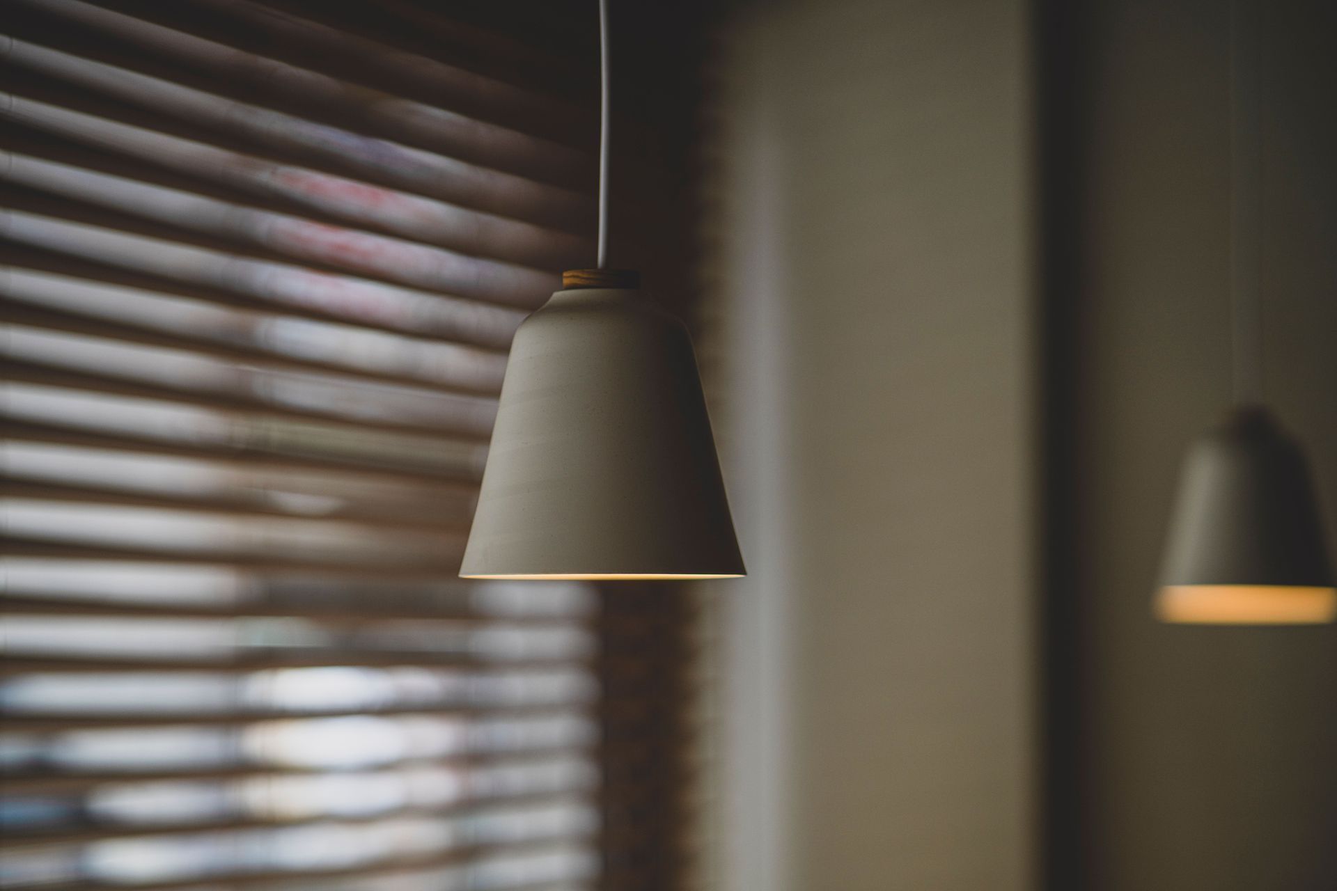 Two hanging lamps beside a window with closed blinds in a softly lit room