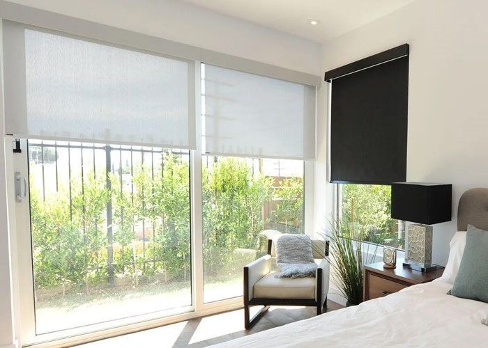 Bedroom with window blinds; large sliding door overlooks a yard. A chair and nightstand are visible.