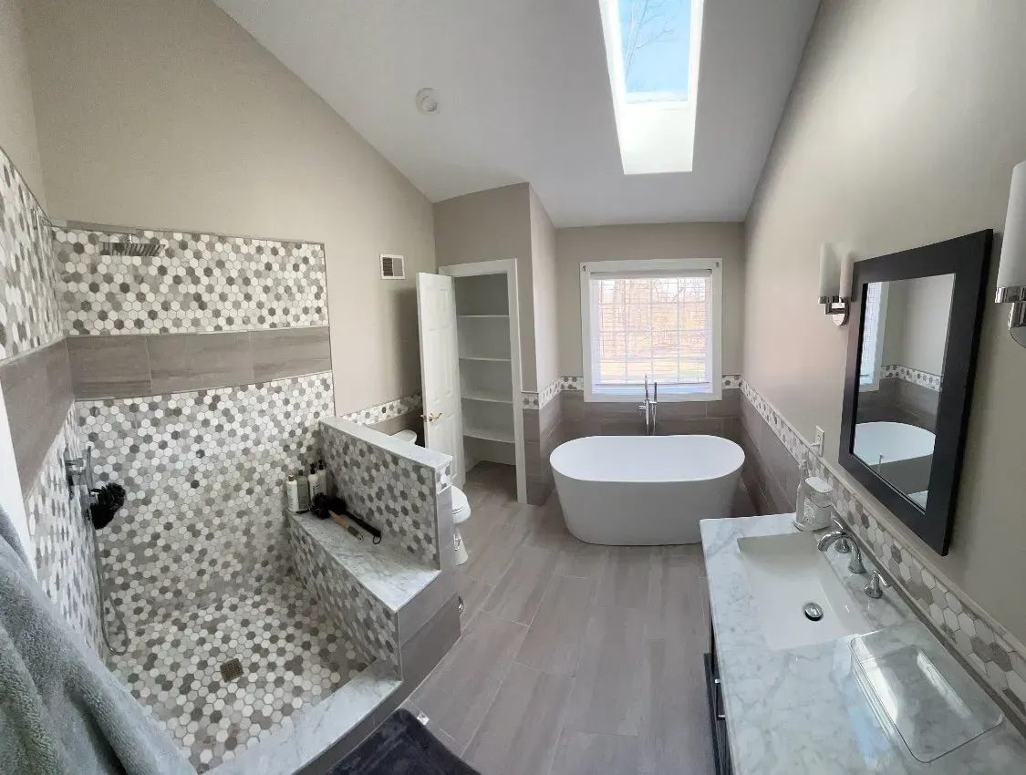 A bathroom with a tub , sink , shower and skylight.