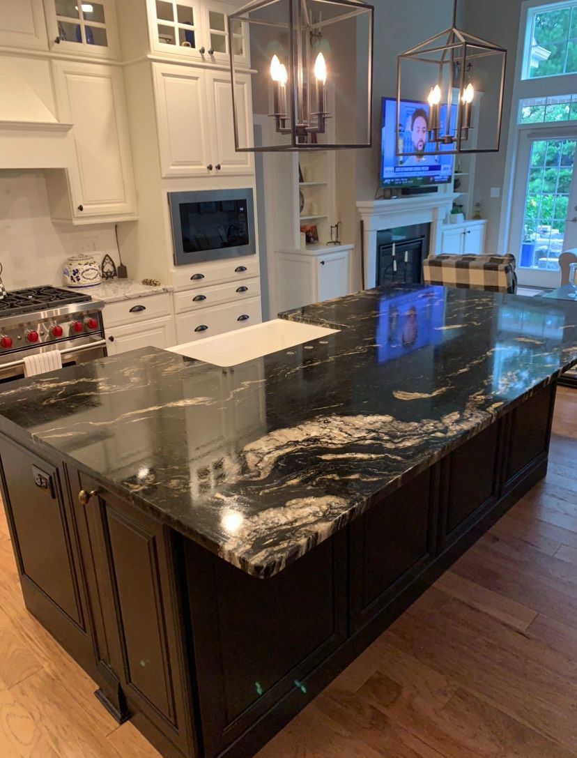 A kitchen features a large, dark-marbled island with black cabinetry, white upper cabinets, and two pendant lanterns.