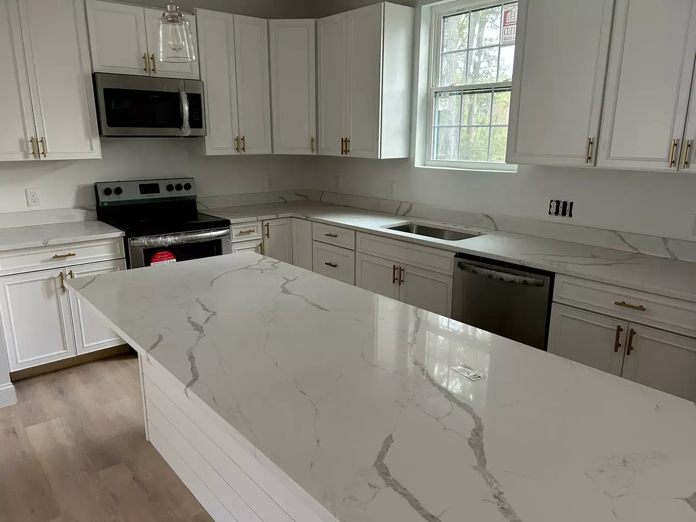 A kitchen with white cabinets , stainless steel appliances , and marble counter tops.