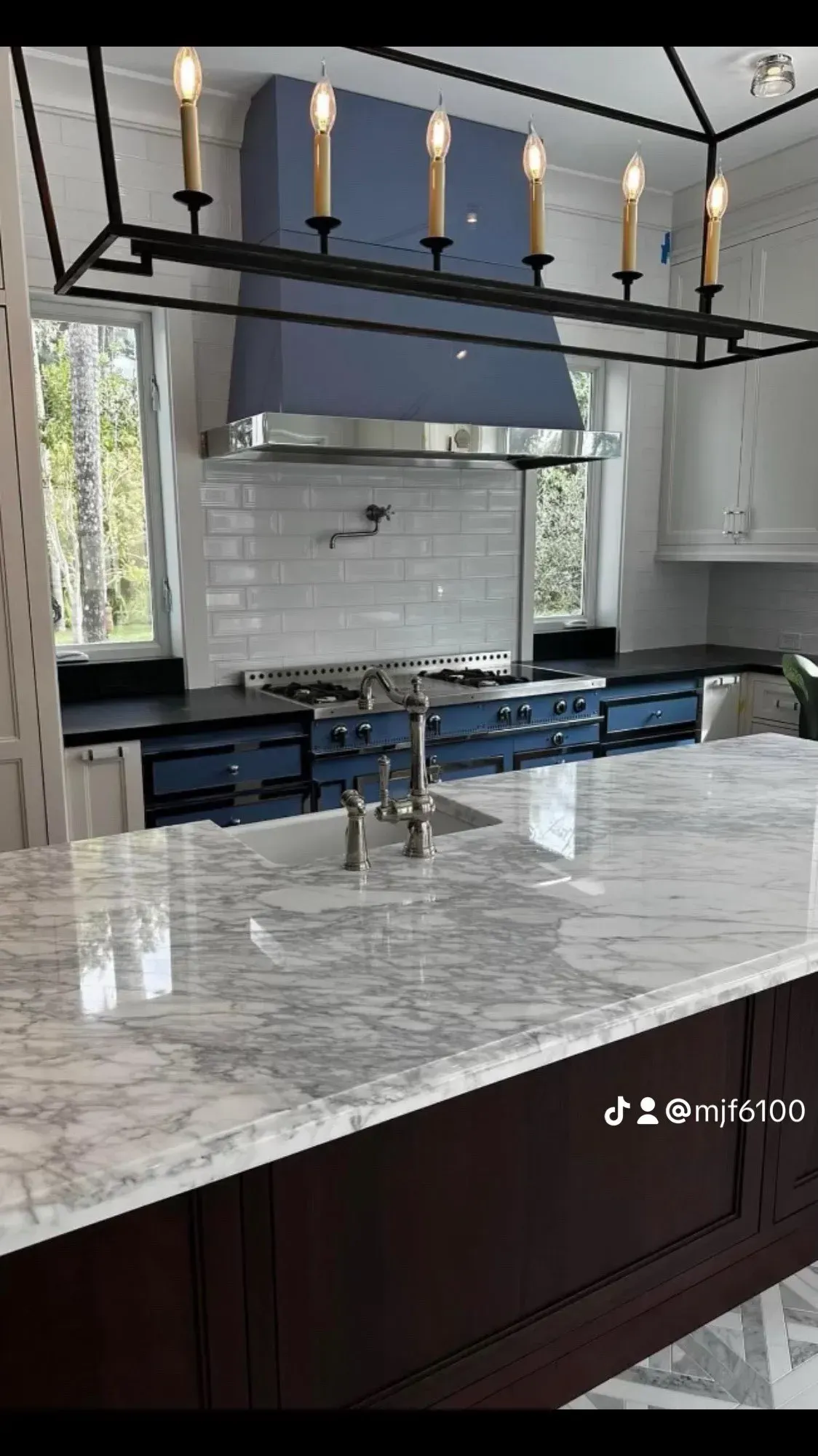 A kitchen with a large island , sink , stove and hood.