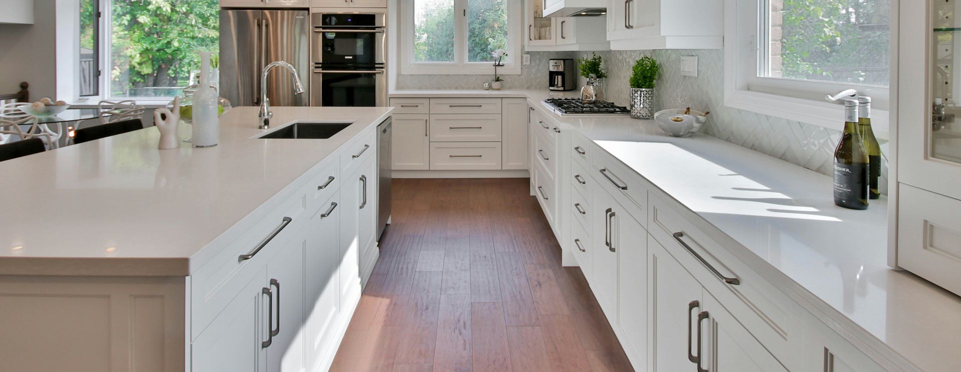 A kitchen with white cabinets , white counter tops , stainless steel appliances and hardwood floors.