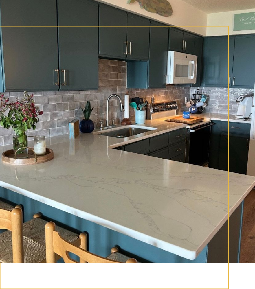 A modern kitchen features dark cabinets, a light stone countertop, a brick backsplash, and two wooden stools.