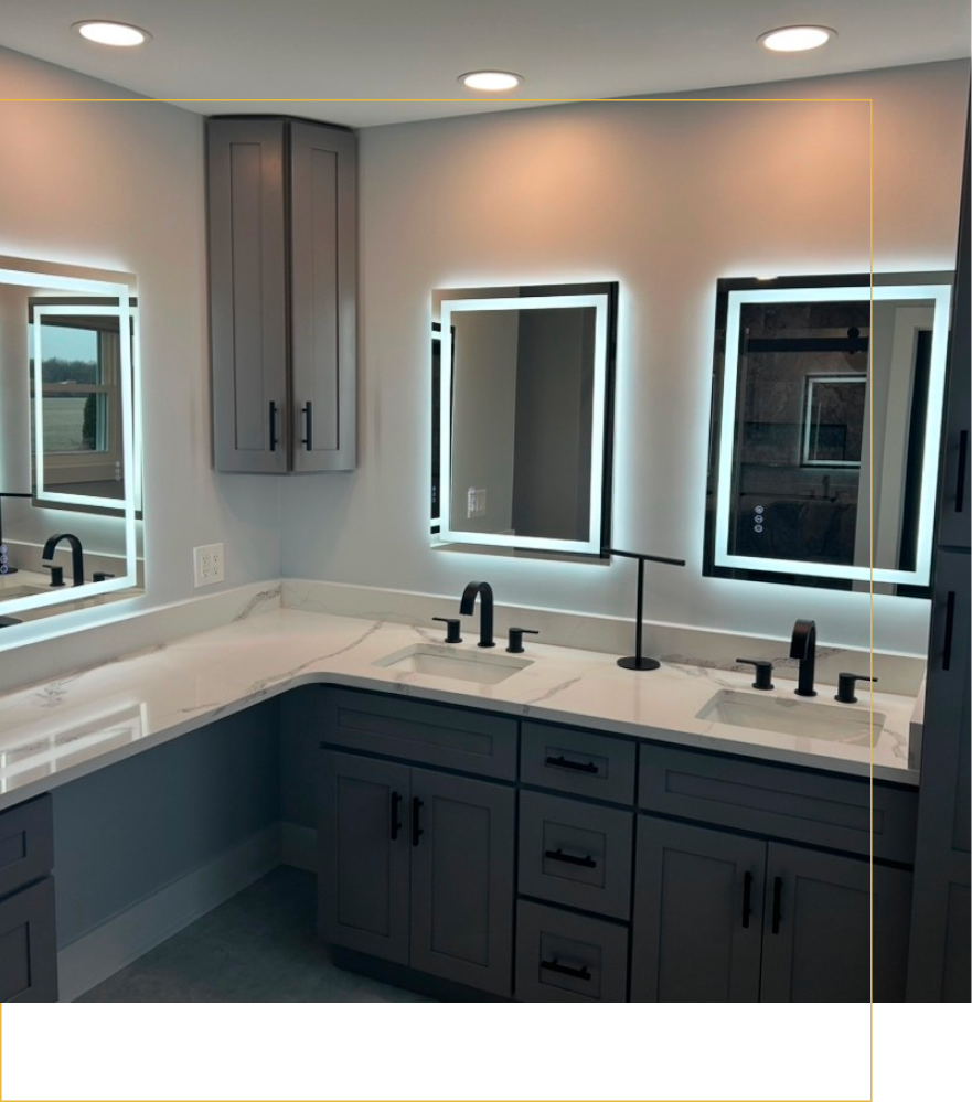 A modern bathroom vanity with grey cabinets, white marble countertops, two square sinks, and lit, rectangular mirrors.