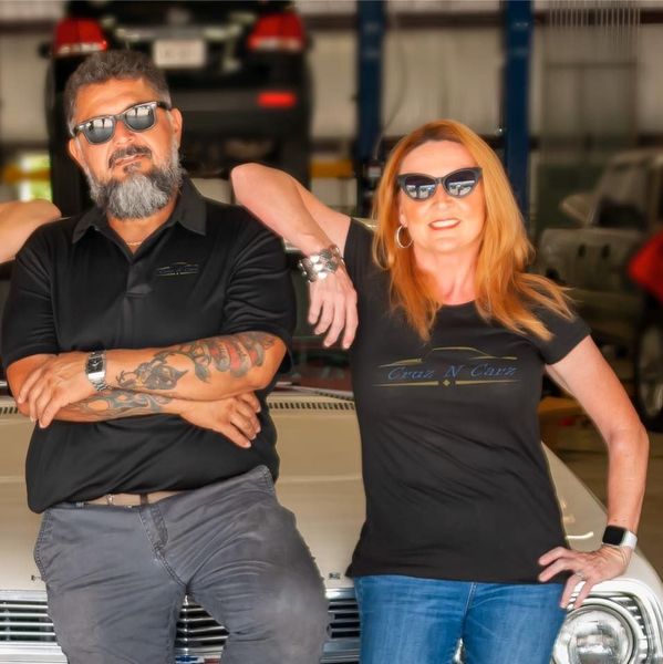 Two people leaning on a car in a garage, both wearing sunglasses and black shirts. | Cruz-N-Carz