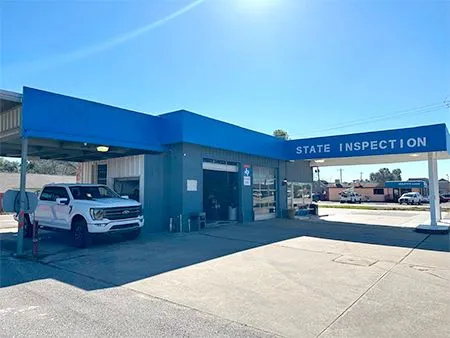 Blue state inspection station with a white pickup truck parked outside under a bright sky | Cruz-N-Carz