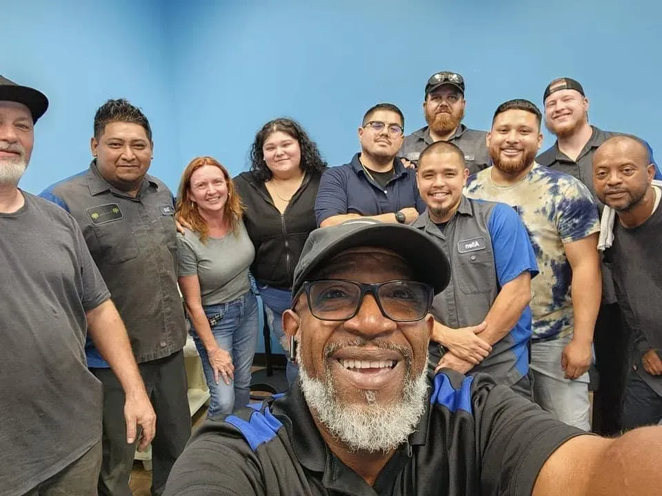 Group selfie of smiling coworkers in casual clothes indoors, with a man in front holding the camera. | Cruz-N-Carz