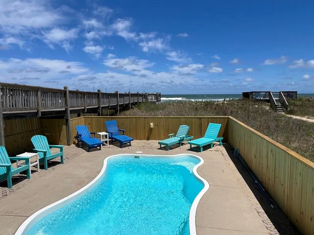 Poolside view: chairs, pool, beach, boardwalk, blue and turquoise, sunny day.