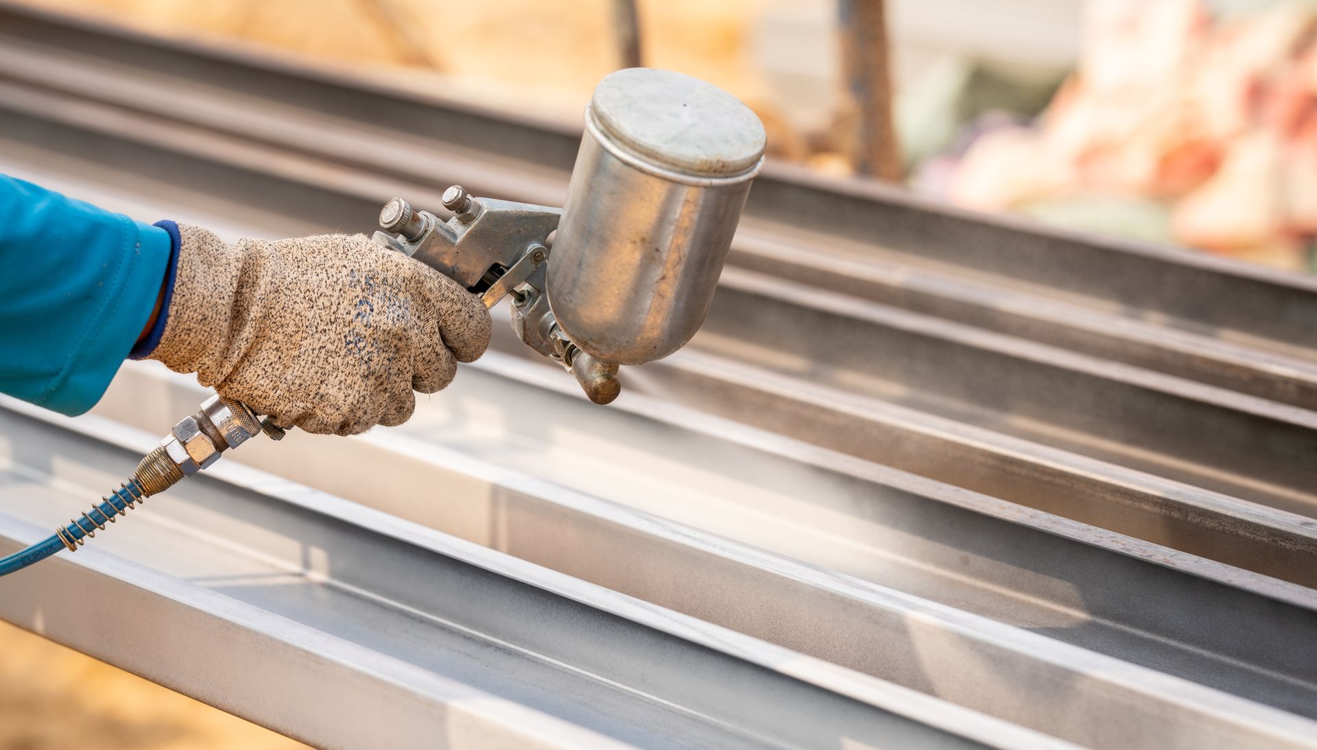 Worker applying a protective metal coating to steel beams with a spray gun.