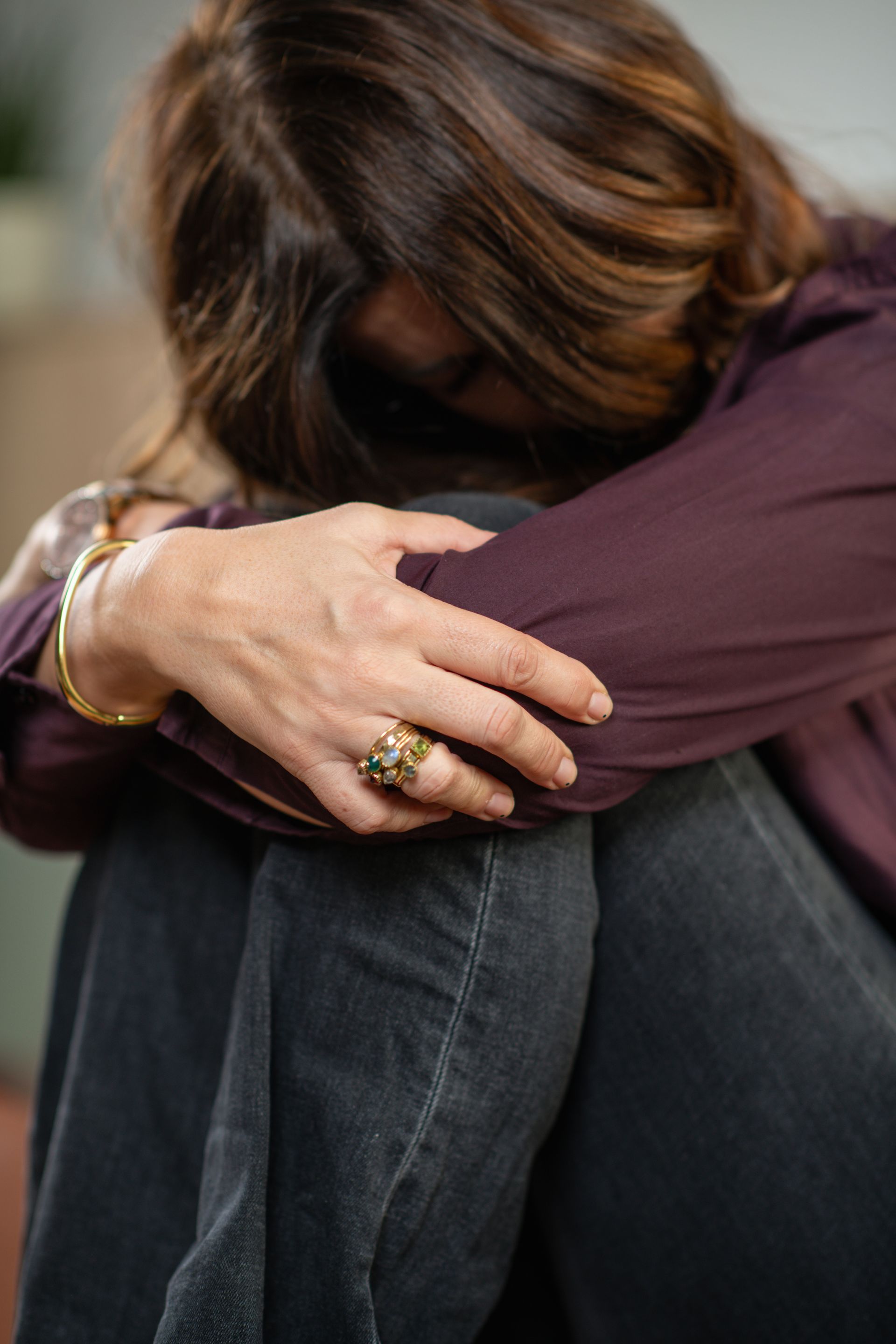 Person hugging another person tightly, seated with arms wrapped around them, wearing a purple top and dark jeans.