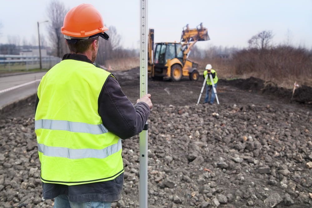 A Construction Worker Is Standing In The Dirt Holding A Pole — Clarence Valley Surveys In Grafton, NSW