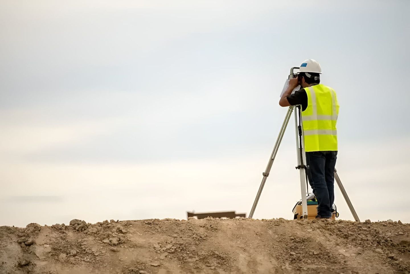 A Man Is Standing On Top Of A Dirt Hill Looking Through A Telescope — Clarence Valley Surveys In Grafton, NSW