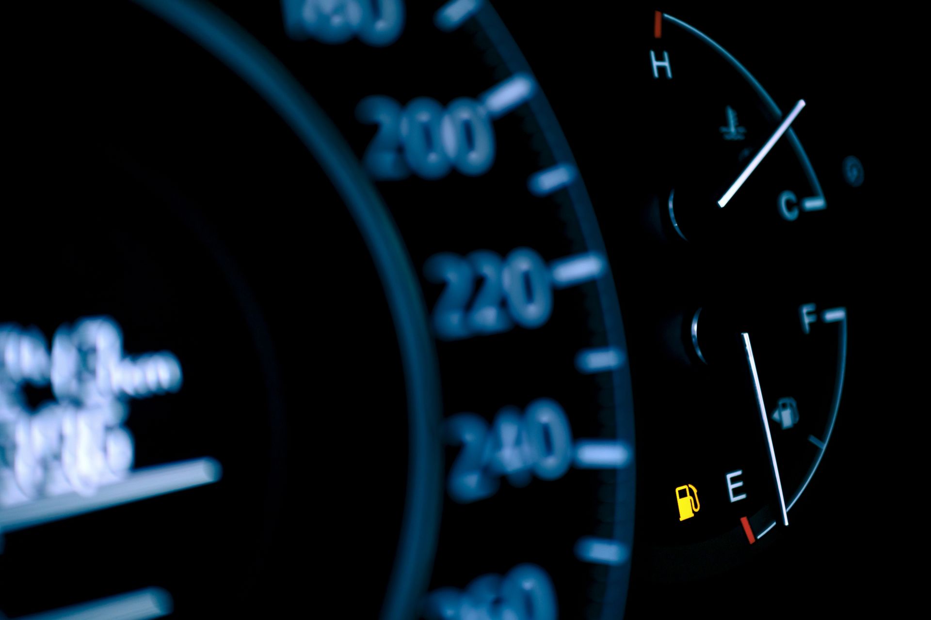 Close-up of car dashboard gauges showing speedometer and low fuel warning icon.