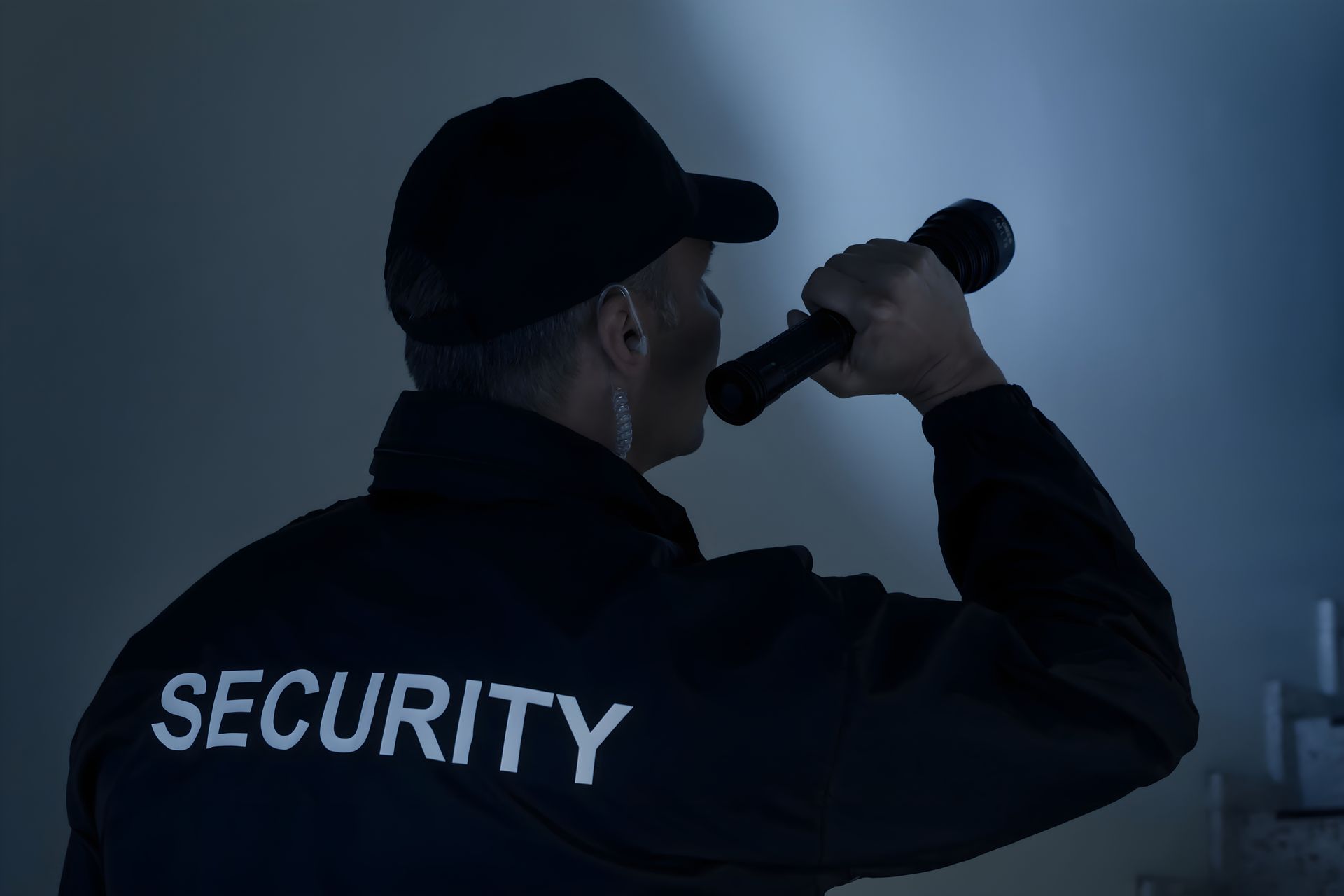 A security guard in a dark uniform holding a flashlight, viewed from behind at night. A security guard in a dark uniform holding a flashlight, viewed from behind at night.