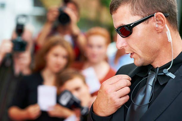 A man in a suit and tie is talking on a walkie talkie in front of a crowd of people.