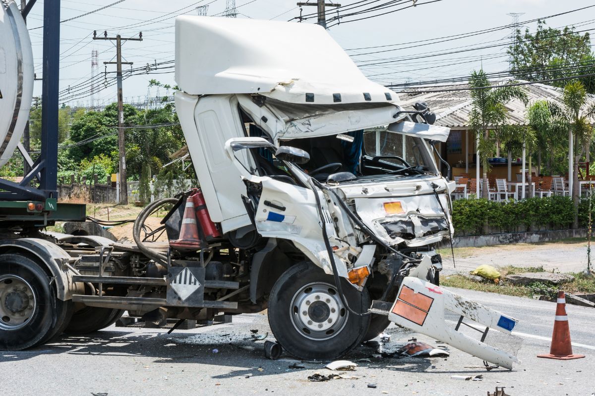 A white semi truck has crashed into a concrete barrier on the side of the road.