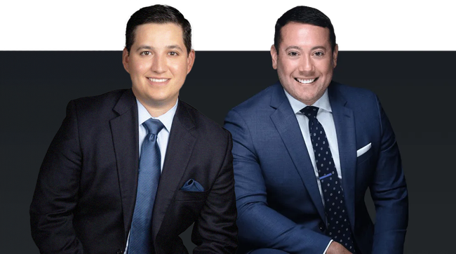 Richard Gonzales and Aaron Rivera in suits and ties are sitting next to each other and smiling.