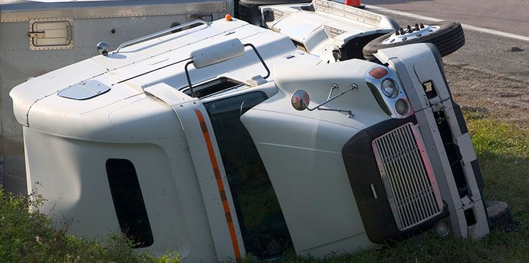 A white semi truck is laying on its side in the grass.