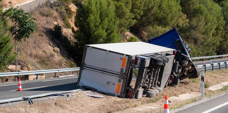 A semi truck has turned over on the side of the road.
