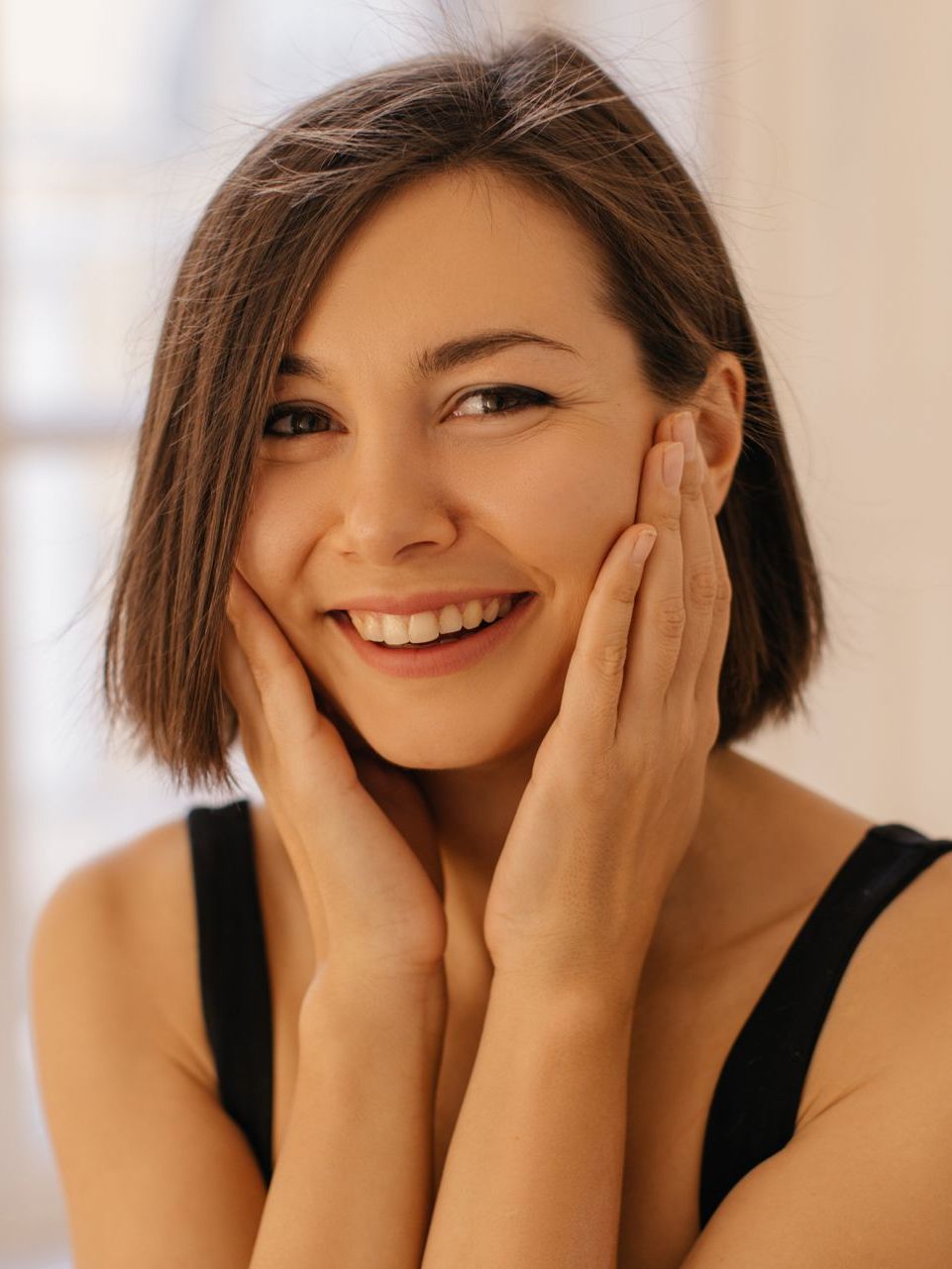 a woman is smiling and touching her face with her hands