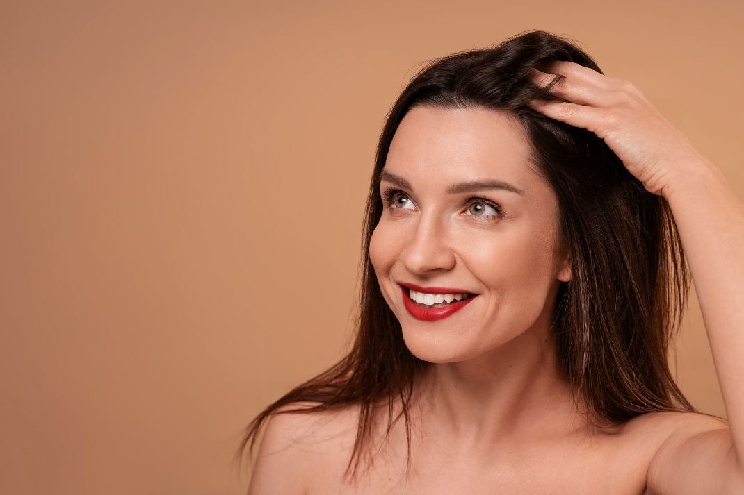 Close-up of a smiling woman massaging her scalp with her left hand.